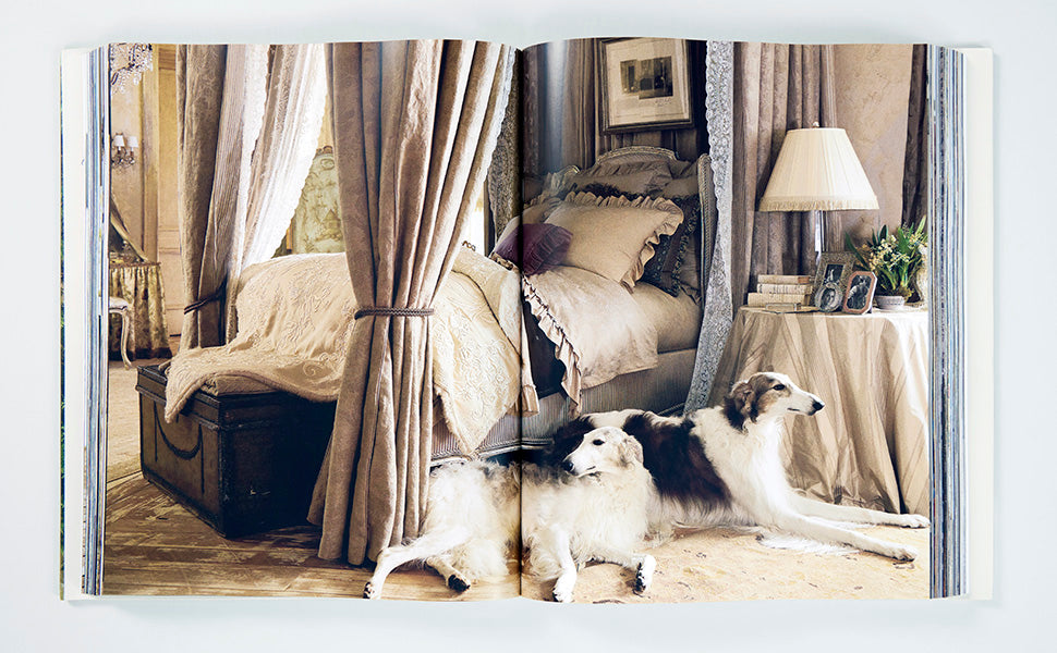 Two long-haired dogs lie on the floor beside a canopied bed in a lavishly decorated bedroom with neutral tones and elegant furnishings, capturing the refined aesthetic showcased in *Ralph Lauren: A Way of Living* by Rizzoli.