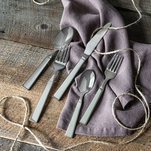 The Simon Pearce Woodstock 5-Piece Flatware Setting—two forks, two spoons, and a knife—is displayed on rustic wood with a purple napkin and twine, ideal for modern tables.
