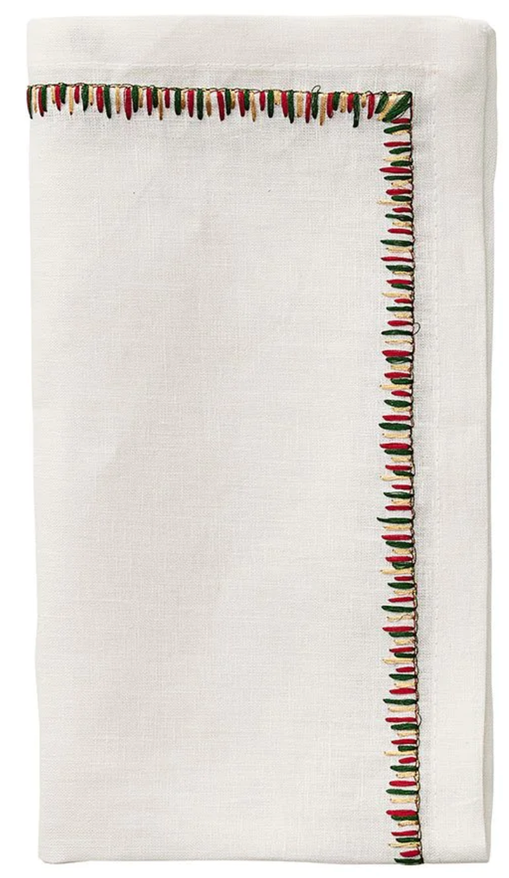 The Kim Seybert Filament Napkin Set features a folded white linen napkin with exquisite red, green, and black embroidered stitching along the edge.