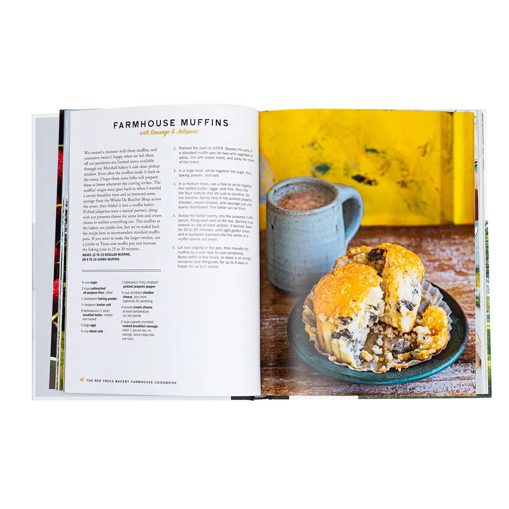 The open Red Truck Bakery Cookbook by Penguin Random House displays a farmhouse muffins recipe on the left page and a photo of muffins alongside a mug of coffee on the right, all set against a cheerful yellow background—evoking the cookbook’s signature warmth and charm.