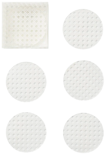 Six white, circular textured pads are shown, with one pad stored in a square white container in the top left corner. These Kim Seybert Reed Coasters with Caddy, White, Set of 6 add a touch of elegance to any outdoor dining experience.