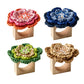 Four Kim Seybert Pareo Napkin Rings, each topped with a hand-crocheted flower in pink, blue, green, or tan, are arranged in a grid on a white background.