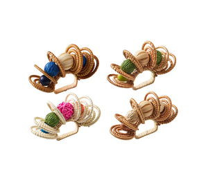 Four Calypso Napkin Rings by Kim Seybert, featuring woven rattan, hand-dyed wooden beads, and colorful yarn balls, artfully arranged on a white background.