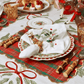 A Merry and Bright Tablecloth by Kim Seybert featuring red ribbons and greenery, set with a plaid placemat, an embroidered holiday napkin, a reindeer napkin ring, and bamboo flatware.