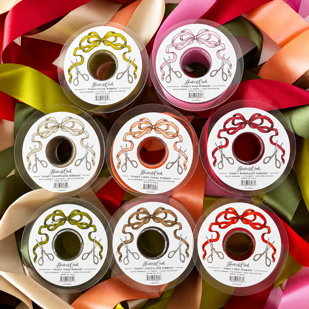 Nine spools of Fancy Ribbon in various colors, including a lovely olive ribbon, are arranged in a square pattern and viewed from above. Each spool features a label with a bow illustration and the brand name “Hester & Cook,” making them perfect for gift wrapping.