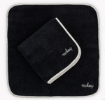 The Matouk Giza Makeup Towel Set features two black, fade-resistant towels with white "makeup" embroidery—one flat, one folded—adding a chic touch to your vanity.