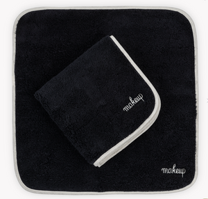 The Matouk Giza Makeup Towel Set features two black, fade-resistant towels with white "makeup" embroidery—one flat, one folded—adding a chic touch to your vanity.