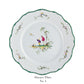 White dinner plate from the Longjiang Dinnerware Collection by Raynaud features scalloped green edge, floral details, and a central scene of two figures under a tree. Text below reads "Dinner Plate No. 4." Perfect for timeless faience-style dinner services.