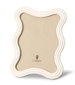 The White Ripple Enamel Frame Collection by L'Objet features a wavy-edged off-white enamel border, a beige backing, and the L'Objet logo displayed at the center.