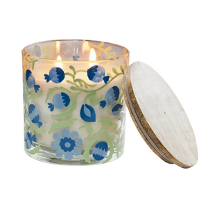 A lit Pondicherry Candle & Incense Collection vetiver candle in a blue and green floral glass jar, shown with its circular wooden lid leaning against the side.