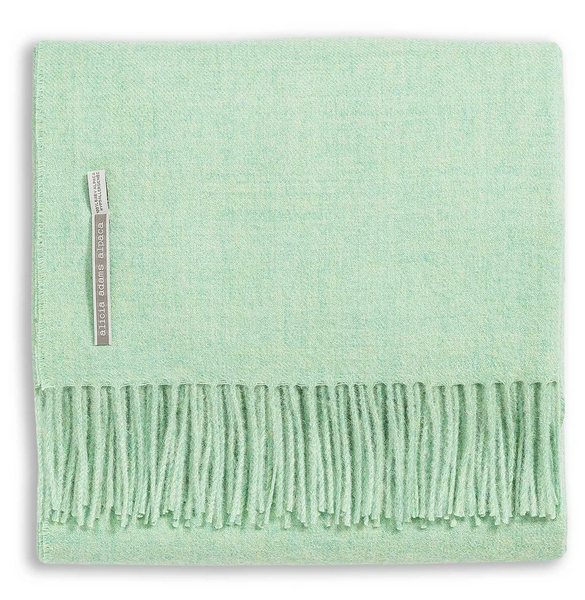 A folded Alicia Adams Alpaca Classic Throw in light green jade, crafted from luxurious baby alpaca with fringed edges and a label near the edge indicating its fair-trade origins.