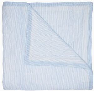 The John Robshaw Nandi Light Indigo Quilt, a folded blue and white striped cotton voile piece, is shown on a white background with one corner turned down to reveal the reverse—showcasing the elegance of traditional Indian quilts.