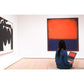 A person sits on a bench in an art gallery with a laptop, facing “Rothko” by Chronicle Books—a striking abstract painting dominated by red and dark hues evocative of classic color field works. Another black and white Abstract Expressionism artwork is displayed on the left wall.