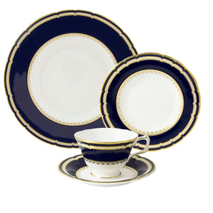 The Ashbourne Navy Dinnerware Collection by Royal Crown Derby is a four-piece fine bone china set with dark blue and gold trim, featuring a dinner plate, salad plate, teacup, and saucer on a classic white background.