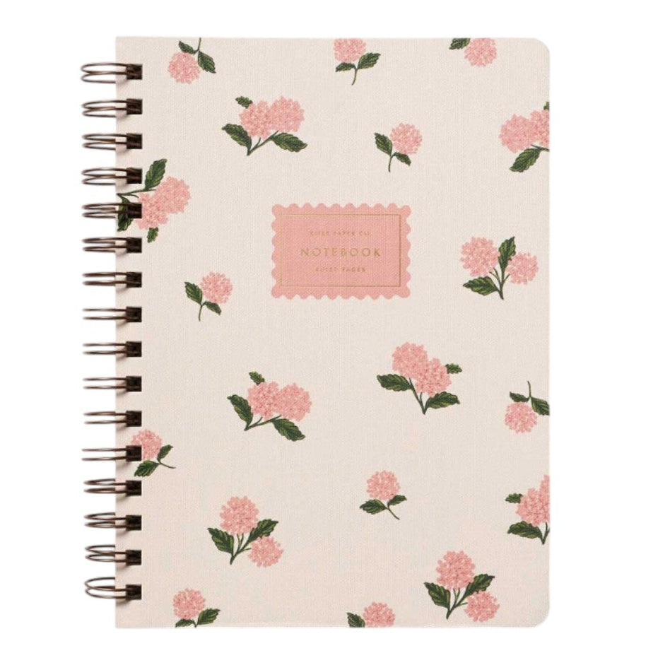The Pink Hydrangea Collection spiral-bound notebook by Rifle Paper Co. features a cream cover with pink hydrangeas and green leaves, plus a central "NOTEBOOK" label—ideal for anyone who loves elegant paper goods.
