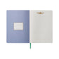 The Aster Softcover Journal by Rifle Paper Co. features a light blue inside cover with a label, lined cream pages adorned with a gold floral design at the top, and a green ribbon bookmark.