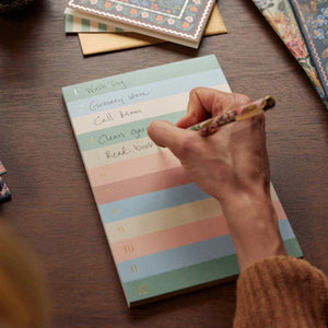Using the Rifle Paper Co. Muted Numbered Color Block Memo Notepad, someone lists tasks—like walking the dog, grocery shopping, and reading—on tear-off sheets for easy daily organization.