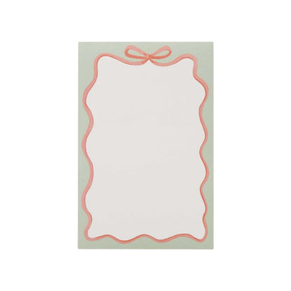 The Rifle Paper Co. Ribbon Notepad features a blank notecard with a scalloped pink border, bow design, and mint accents on a light green background.
