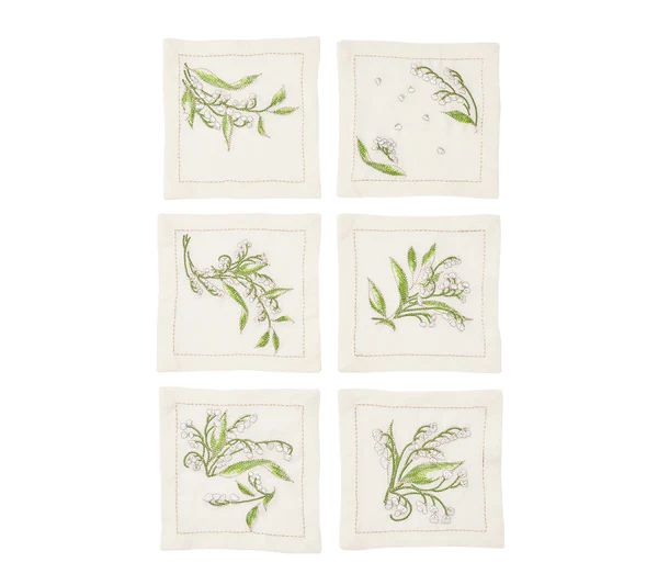 The Kim Seybert Vale Cocktail Napkin Set includes six square, cream linen napkins, each with a distinct green botanical embroidery such as Lily of the Valley, arranged in two rows of three on a white background.