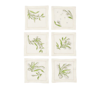 The Kim Seybert Vale Cocktail Napkin Set includes six square, cream linen napkins, each with a distinct green botanical embroidery such as Lily of the Valley, arranged in two rows of three on a white background.