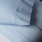Close-up of the Nandi Light Indigo Sheet Set by John Robshaw, featuring blue and white pinstripes, two pillows, and a blanket with hand-embroidered edges, crafted from organic cotton in India.