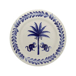 The Casa Deep Navy Dinnerware Collection by Johanna Ortiz features a white plate with a blue leafy border, two blue monkeys, and a coconut palm, all handcrafted from Carmen de Viboral clay and expertly hand-painted.