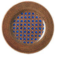 The Patagonia Blue Melamine Dinnerware Collection by Mario Luca Giusti features a round plate with a woven rattan-patterned rim and geometric blue-brown lattice center, blending antique charm with modern style.