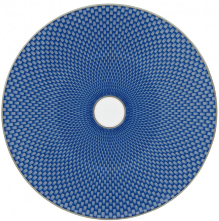 The Raynaud Tresor Blue Dinnerware Collection features round porcelain plates with hand-painted blue geometric patterns radiating from a white center, creating an elegant optical illusion effect for any setting.