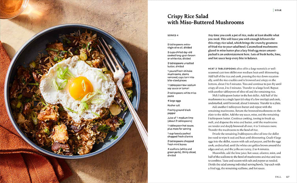 A bowl of rice salad topped with sautéed mushrooms, chopped greens, sunflower seeds, and a sunny-side-up egg sits beside a copy of Salad Seasons by Rizzoli—an inspiring scene for anyone seeking healthy salads or flipping through this beloved cookbook for new vegetable recipes.