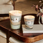 Two Baobab Collection Sand Sonora candles on a wooden coffee table, alongside a book and floral decoration, in a cozy indoor setting.