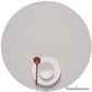A white bowl and plate with a red spoon rest on a Chilewich Round Placemat, crafted from phthalate-free Terrastrand yarns in the Sandstone color.