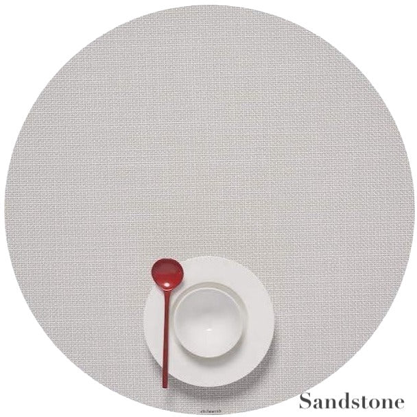 A white bowl and plate with a red spoon rest on a Chilewich Round Placemat, crafted from phthalate-free Terrastrand yarns in the Sandstone color.