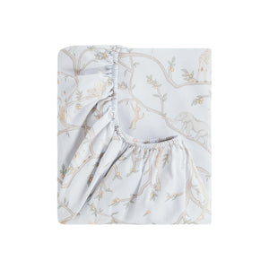 The Gooselings Animal Parade Blue Bedding is a folded fitted sheet with safari animals and tree branches in neutral tones on a light background, made from breathable, pure materials and OEKO-TEX certified for safe and comfortable baby bedding.