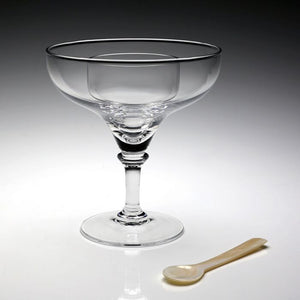 The William Yeoward Crystal Sasha Seafood/Caviar Server, a clear handmade dish with a wide rim, is displayed beside a small beige spoon on a white surface.