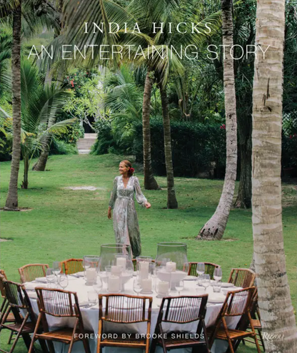 Set amid lush palm trees and verdant lawns, a woman in a flowing dress stands near a grand outdoor table elegantly arranged for a meal—an inviting scene that channels the dreamy tablescapes of *An Entertaining Story* by Rizzoli, where every gathering is steeped in charm and the warmth of cherished family memories.
