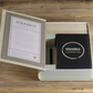 The Scrabble Vintage Bookshelf Edition by WS Game Company is open, revealing its contents including wooden letter tiles and a 1948 vintage-style game board housed inside a fabric-wrapped book. The set is placed on a wooden surface.