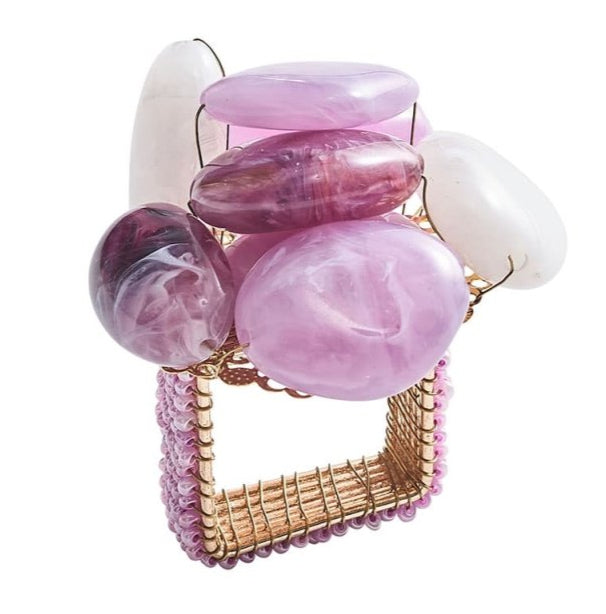 The Kim Seybert Sea Stone Napkin Ring features a gold wire design with a square base, accented by pink and purple polished beads and beach stones for an elegant coastal style.