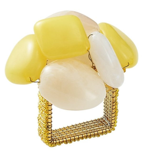 The Kim Seybert Sea Stone Napkin Ring features a gold square base adorned with large, smooth yellow and white stones clustered on top, evoking the look of beach pebbles.