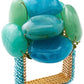 The Kim Seybert Sea Stone Napkin Ring features a square gold design adorned with six large blue and green polished stones, inspired by beach stones, and is accented with small blue beads at the base.