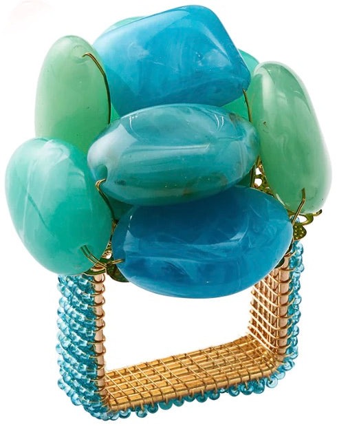 The Kim Seybert Sea Stone Napkin Ring features a square gold design adorned with six large blue and green polished stones, inspired by beach stones, and is accented with small blue beads at the base.