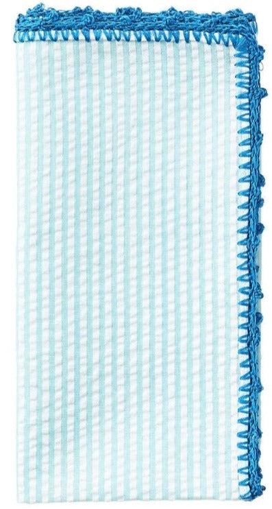 The Kim Seybert Seersucker Napkin Set features light blue and white stripes with a hand-crocheted border, folded neatly.