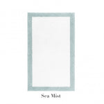 The Graccioza Egoist Border Bath Rug is a rectangular white rug with a light blue-green customizable border, made from soft Egyptian cotton and labeled "Sea Mist" underneath.