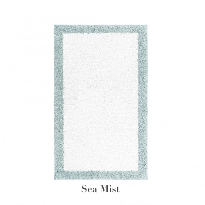 The Graccioza Egoist Border Bath Rug is a rectangular white rug with a light blue-green customizable border, made from soft Egyptian cotton and labeled "Sea Mist" underneath.