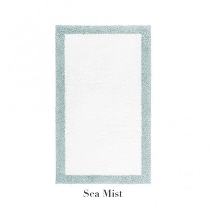 The Graccioza Egoist Border Bath Rug is a rectangular white rug with a light blue-green customizable border, made from soft Egyptian cotton and labeled "Sea Mist" underneath.