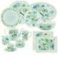 The Aquazzura Casa Secret Garden Dinnerware and Serveware Collection showcases green and blue floral and bird motifs with gold accents on plates, cups, saucers, teapot, sugar bowl, and serving dishes.