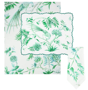 The Aquazzura Casa Secret Garden Table Linen Collection includes a white rectangular tablecloth, placemats, and a folded napkin, all adorned with green botanical and bird illustrations.