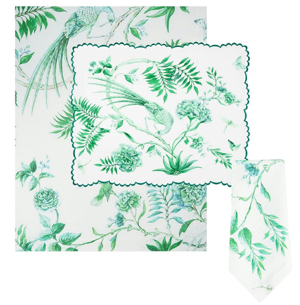 The Aquazzura Secret Garden Linen Collection from Aquazzura Casa features green and white floral-patterned linen napkins and a tablecloth with a Secret Garden motif, complete with birds and lush foliage.