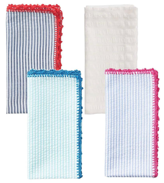 The Kim Seybert Seersucker Napkin Set features four cotton napkins: one white, two striped, and one checkered, all with colorful embroidered edges and a hand-crocheted border in red, blue, and pink.