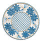 Handcrafted in Colombia, the Serenity Rattan Placemat Collection by Themis Z features round placemats with blue and beige woven patterns, blue floral designs along the rim, and a crisscross center pattern.