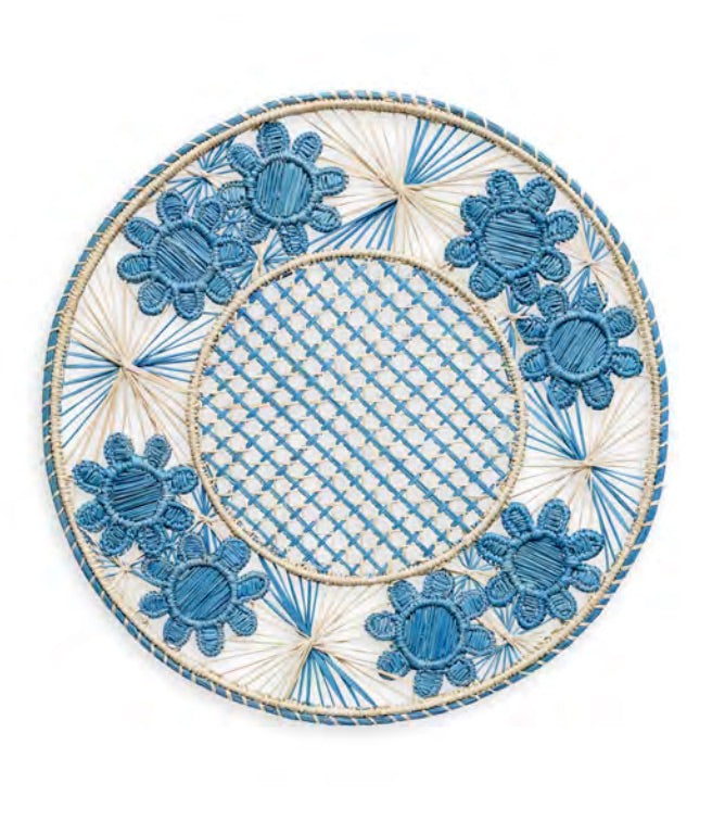 Handcrafted in Colombia, the Serenity Rattan Placemat Collection by Themis Z features round placemats with blue and beige woven patterns, blue floral designs along the rim, and a crisscross center pattern.